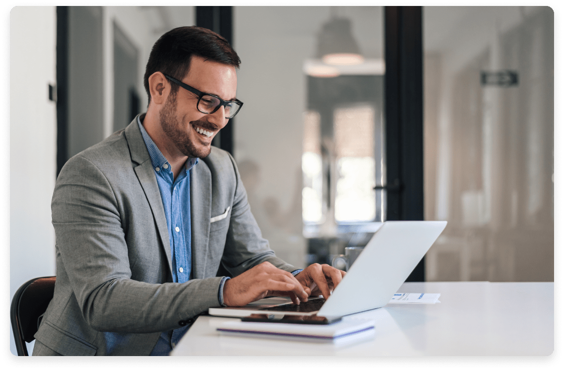 
                  Smiling male professional in smart casual attire working on a laptop in a modern office environment,
                  exemplifying the strategic financial planning and leadership offered by fractional CFO services for consulting firms.
                