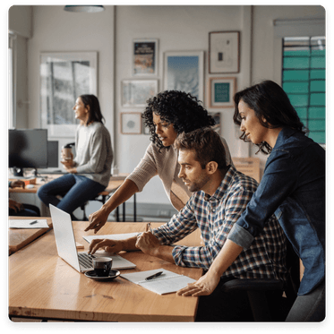 Clickable image: Four tech professionals collaborating at a table with a laptop. Explore accounting expertise for tech companies.